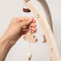 Hand hanging a wooden cloud pendant from the baby play gym arch