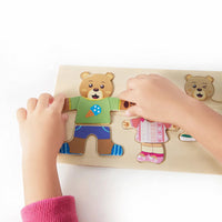 Child's hands dressing the bear figure with puzzle clothing pieces