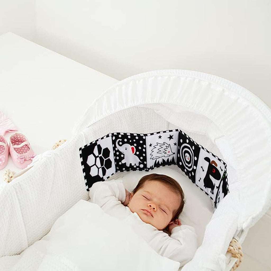 Newborn asleep in a bassinet beside the high-contrast fabric book