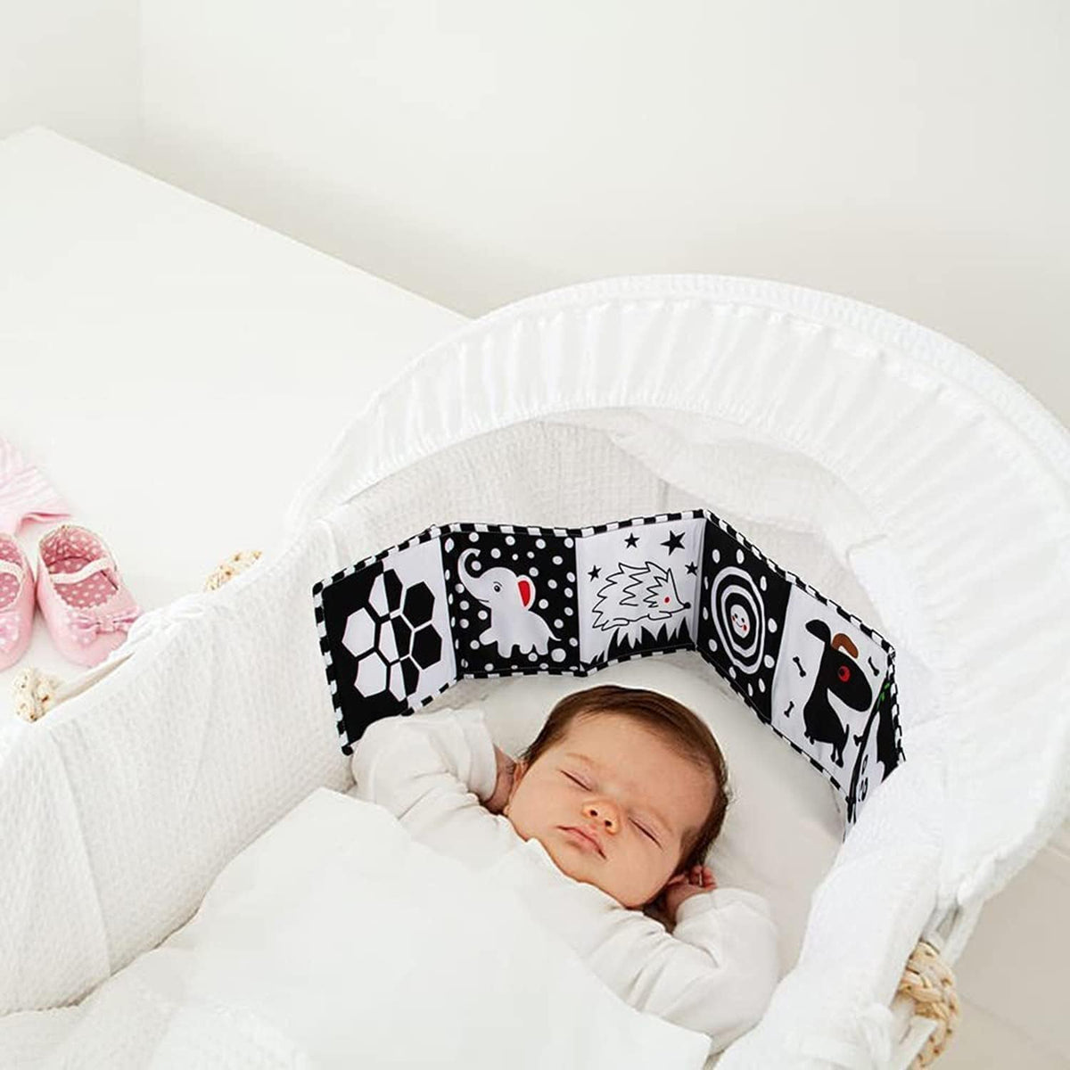 Newborn asleep in a bassinet beside the high-contrast fabric book