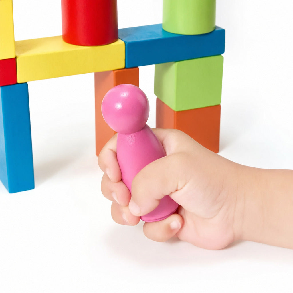 Child's hand gripping a pink wooden peg doll beside a block tower