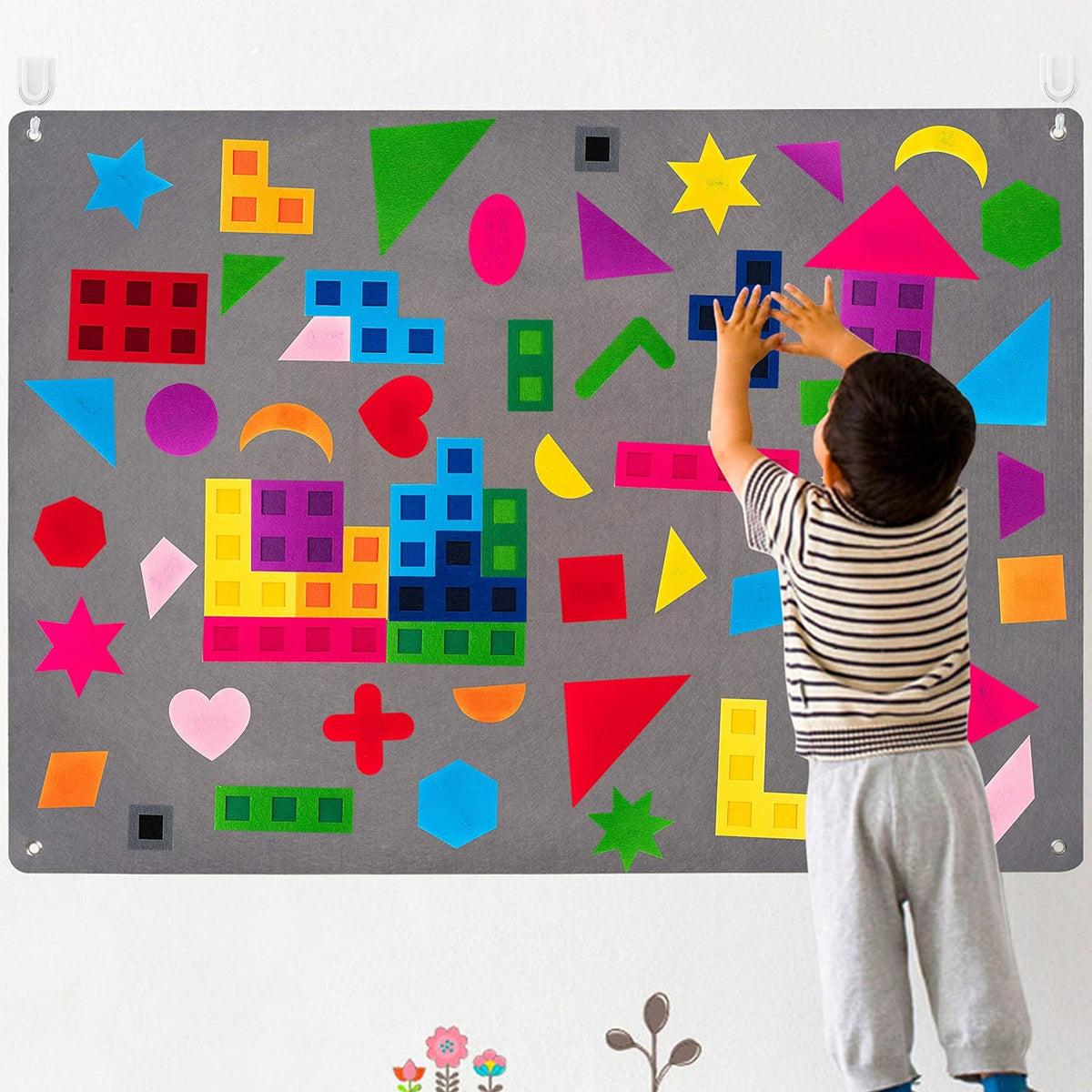 Child placing felt shapes on the large grey wall felt board