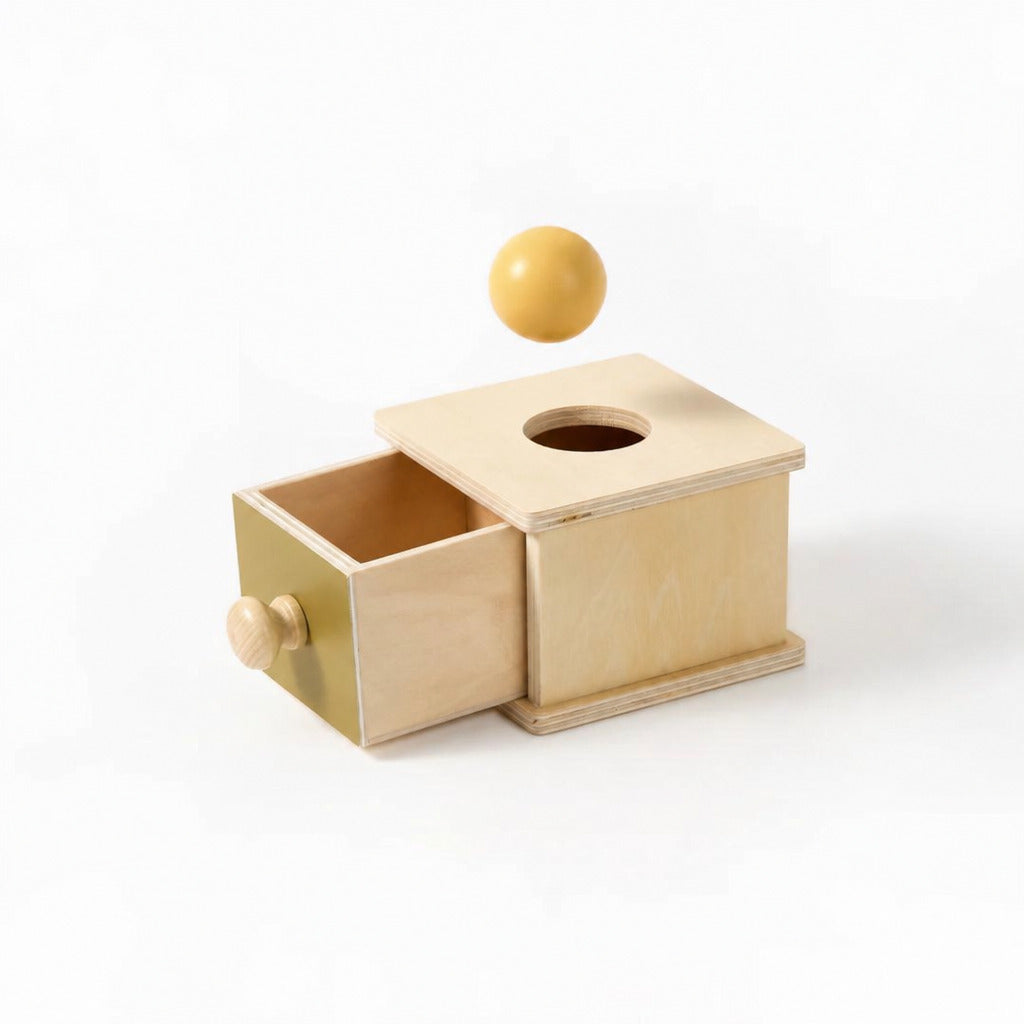 Object permanence box with its drawer open and a ball on top