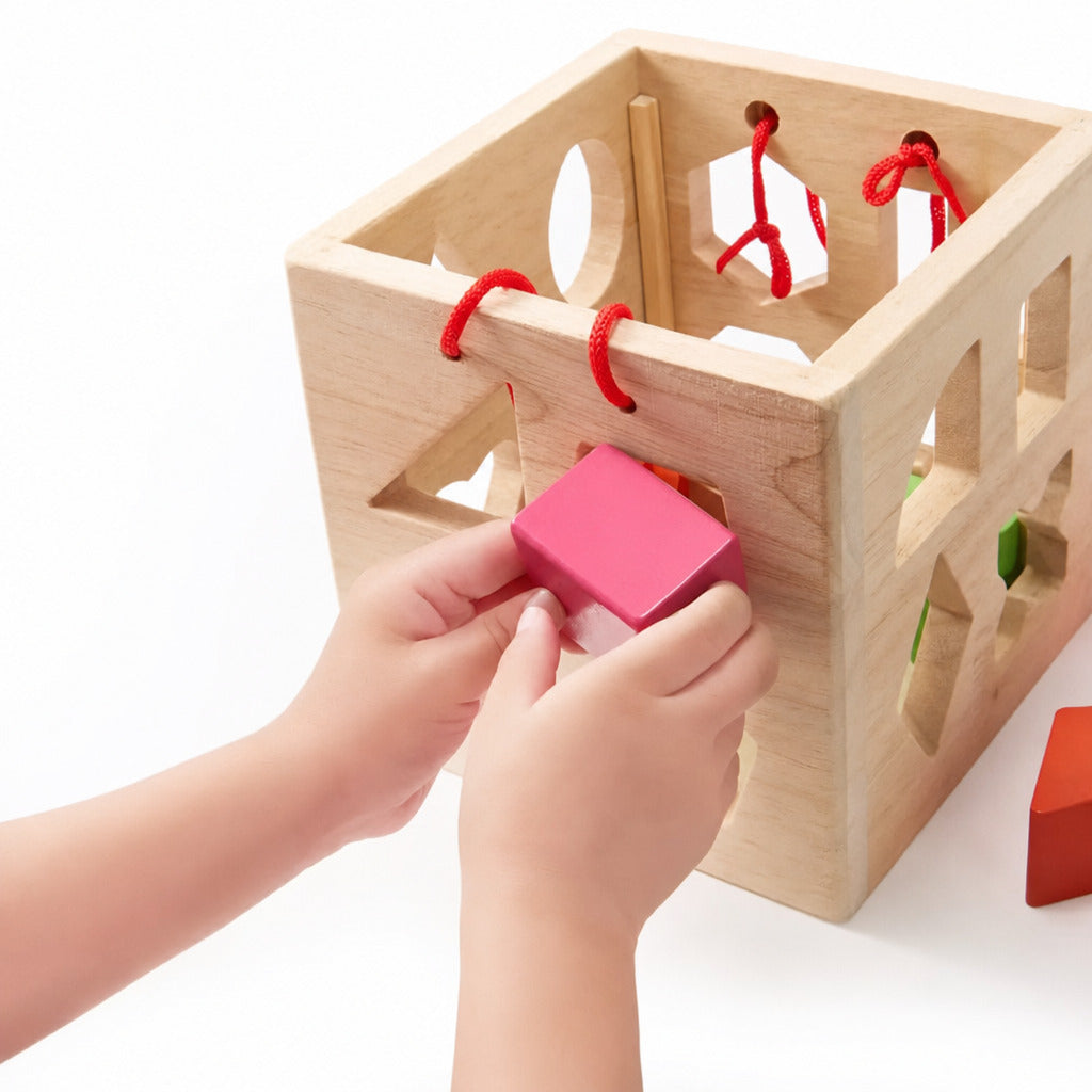 Child's hand feeding a pink block into the shape sorter cube