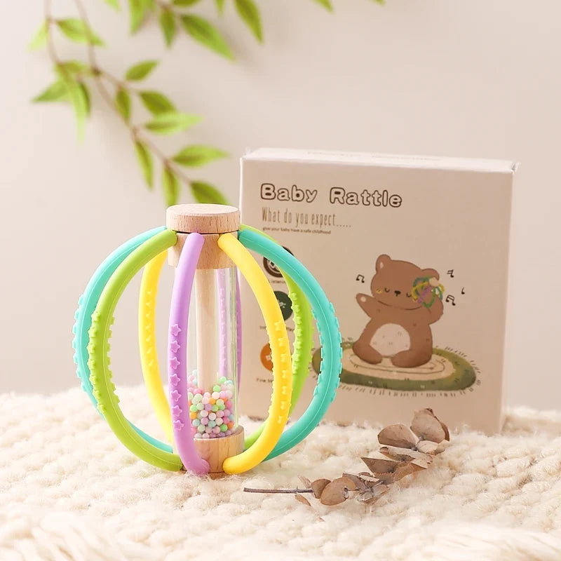 Pastel teething rattle ball with rainbow beads beside its box