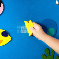 Child's hand pressing a felt fish onto the blue ocean board