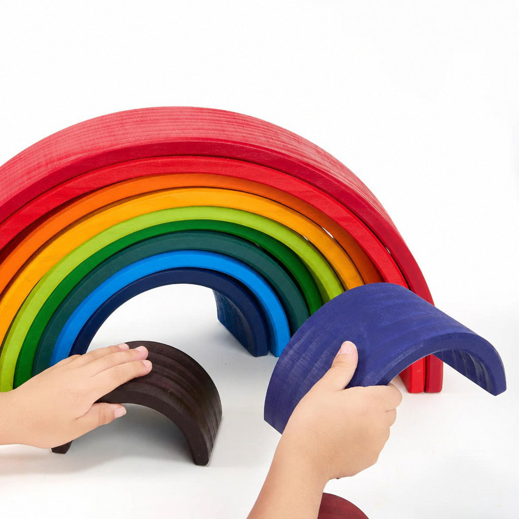 Children's hands placing arches on the large wooden rainbow stacker